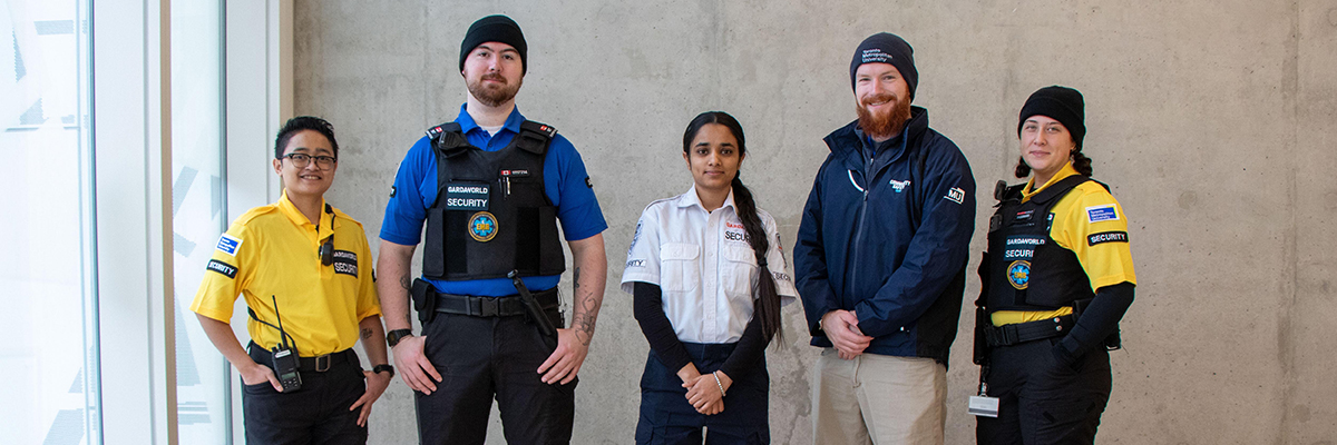 Five members of the Community Safety and Security team wearing the new uniforms and attire in front of a cement wall.