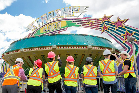 Members of the TMU Thrill Club in hard hats and yellow safety vests looking at a carnival ride.