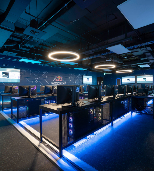 Red Bull Gaming Hub with rows of high performance gaming computers with circular lights above and blue neon lights below.