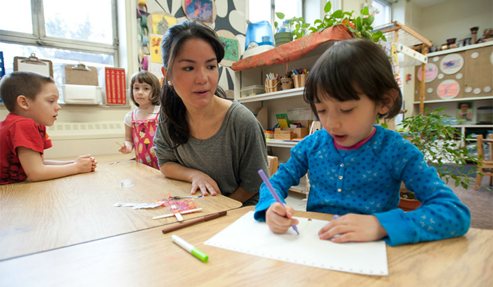 Early childhood educators works with child who is drawing.