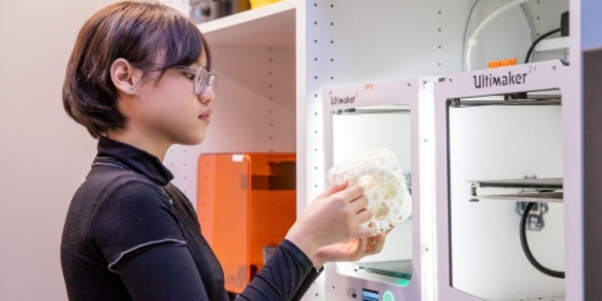 Asian female standing near 3D printer, holding 3D printed object