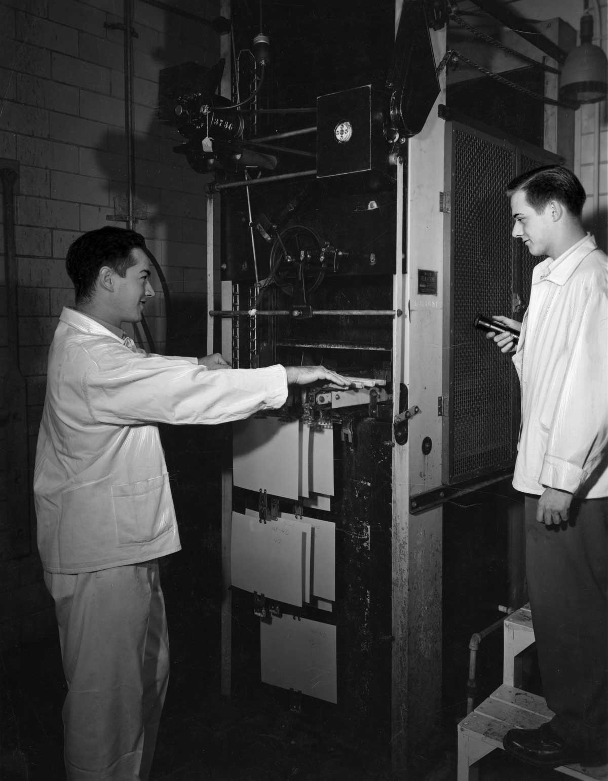 Two men operating a Pako Corporation Filmachine