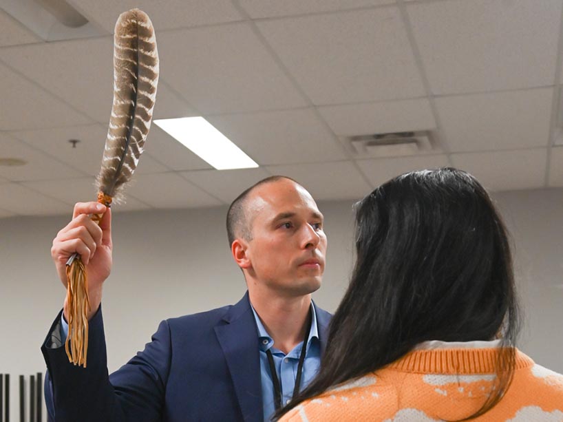 Michael Mihalicz holds a large feather in front of a young woman with her back turned.
