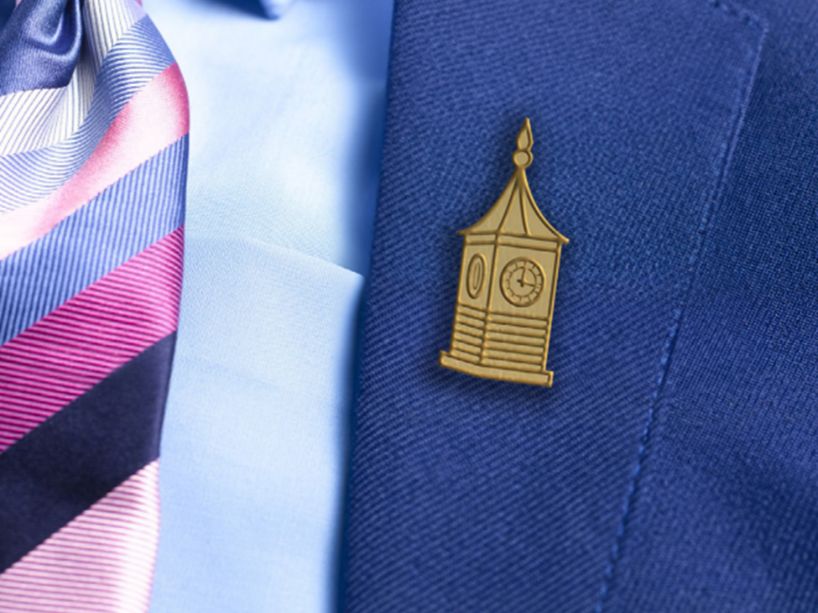 A gold pin of the carillon tower on the lapel of a navy blue suit.