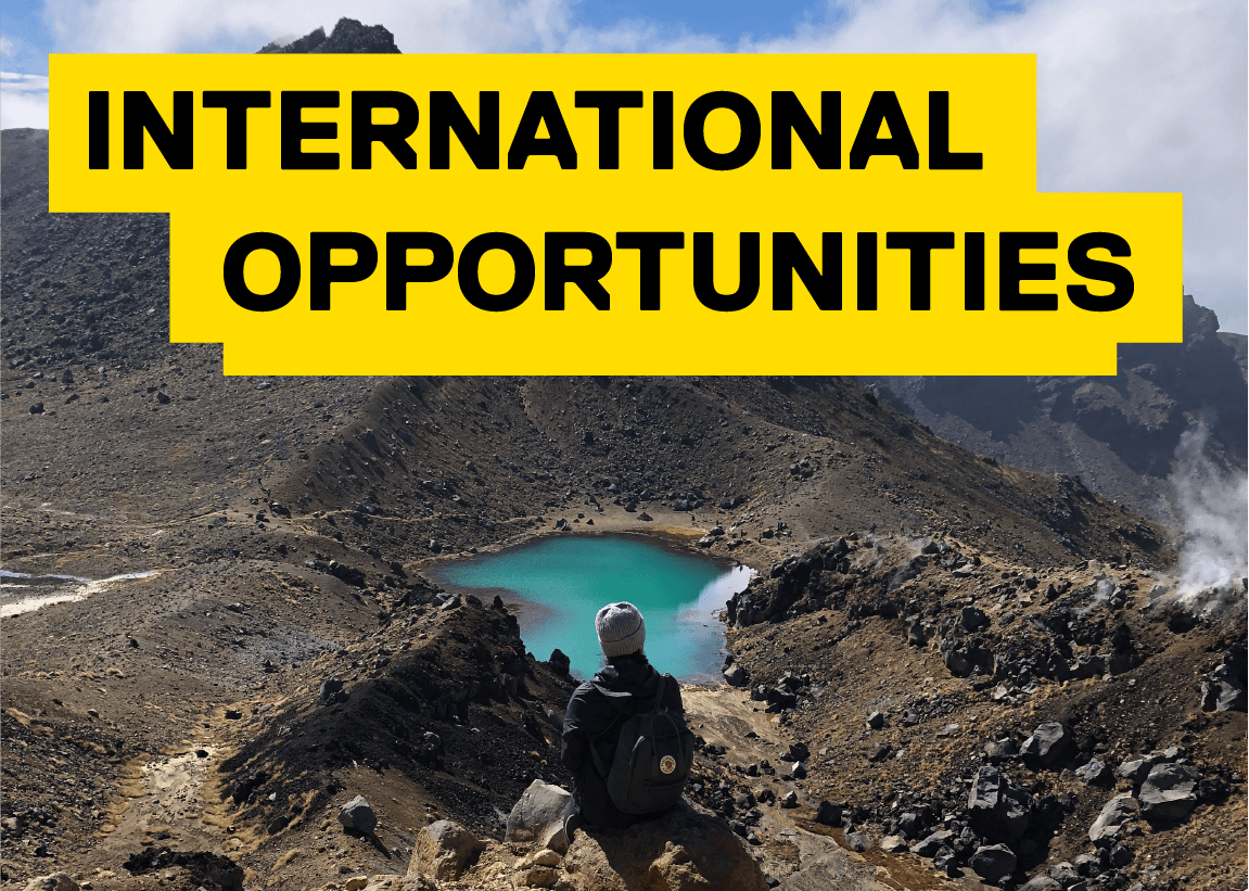 International opportunities in black text on a yello background student sitting on top of a mountain looking dow at a patch of crystal clear blue water 