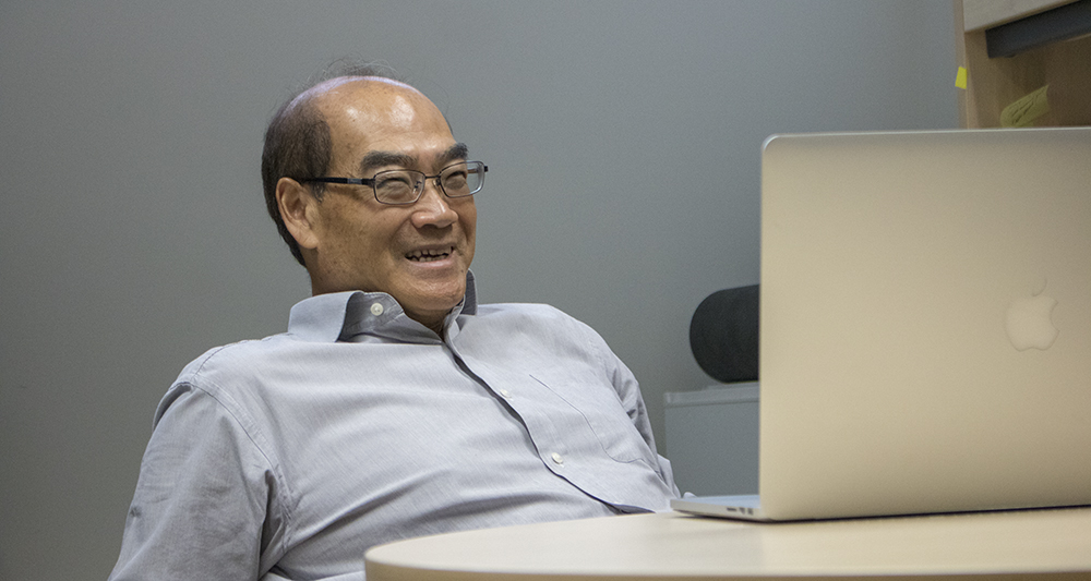 Cheung Poon smiling and sitting at his desk