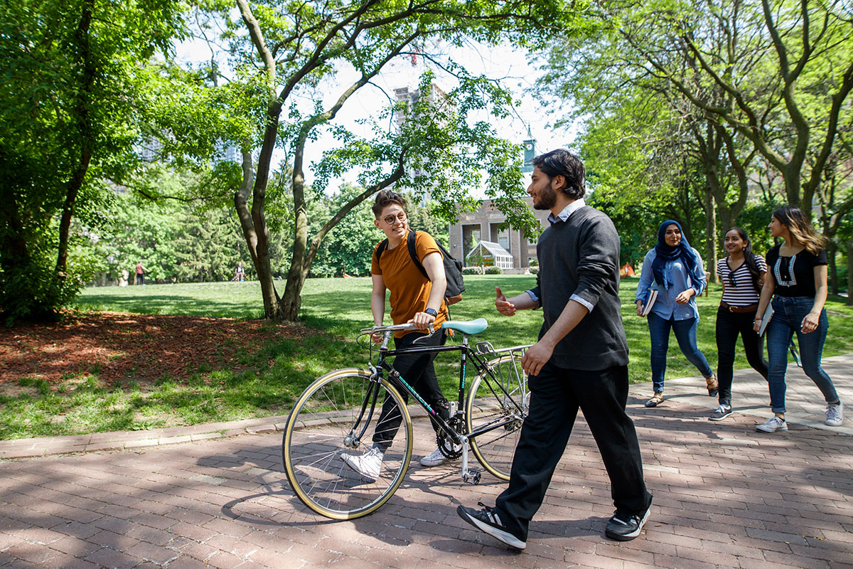 A group of students are walking and engaging in conversations at the quad. One of the students is walking with a bike.