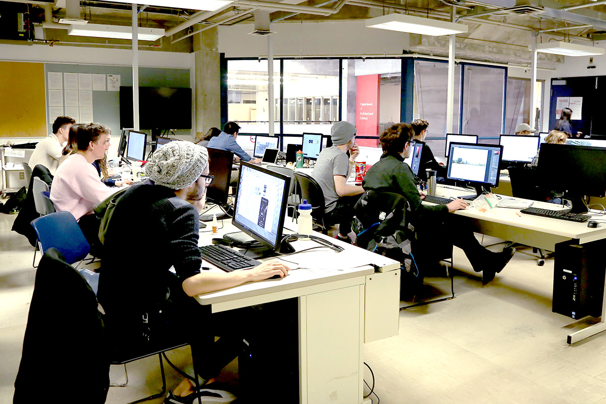Around 10 students work on desktop computers located on long, communal desks.