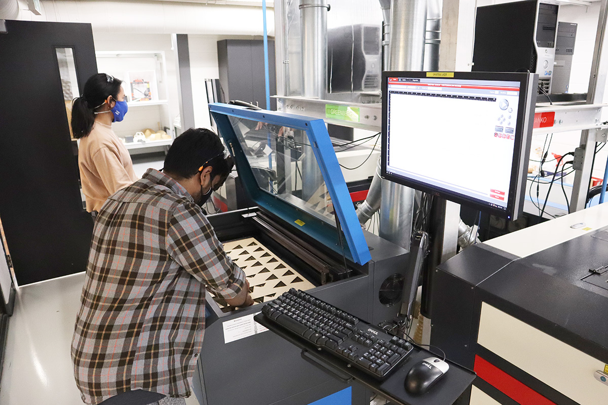 In the Digital Fabrication Lab, a student works on a design using a laser cutting machine, which is connected to a computer monitor. 