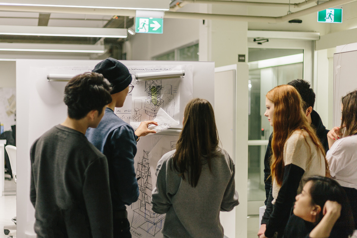 Group of students critiquing architectural blueprints hanging on the wall