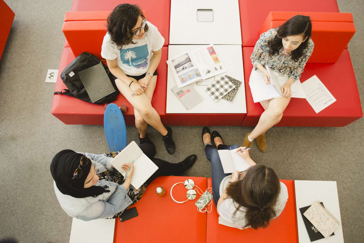 Four student sitting on red chairs at the SLC, facing each other and discussing a project.