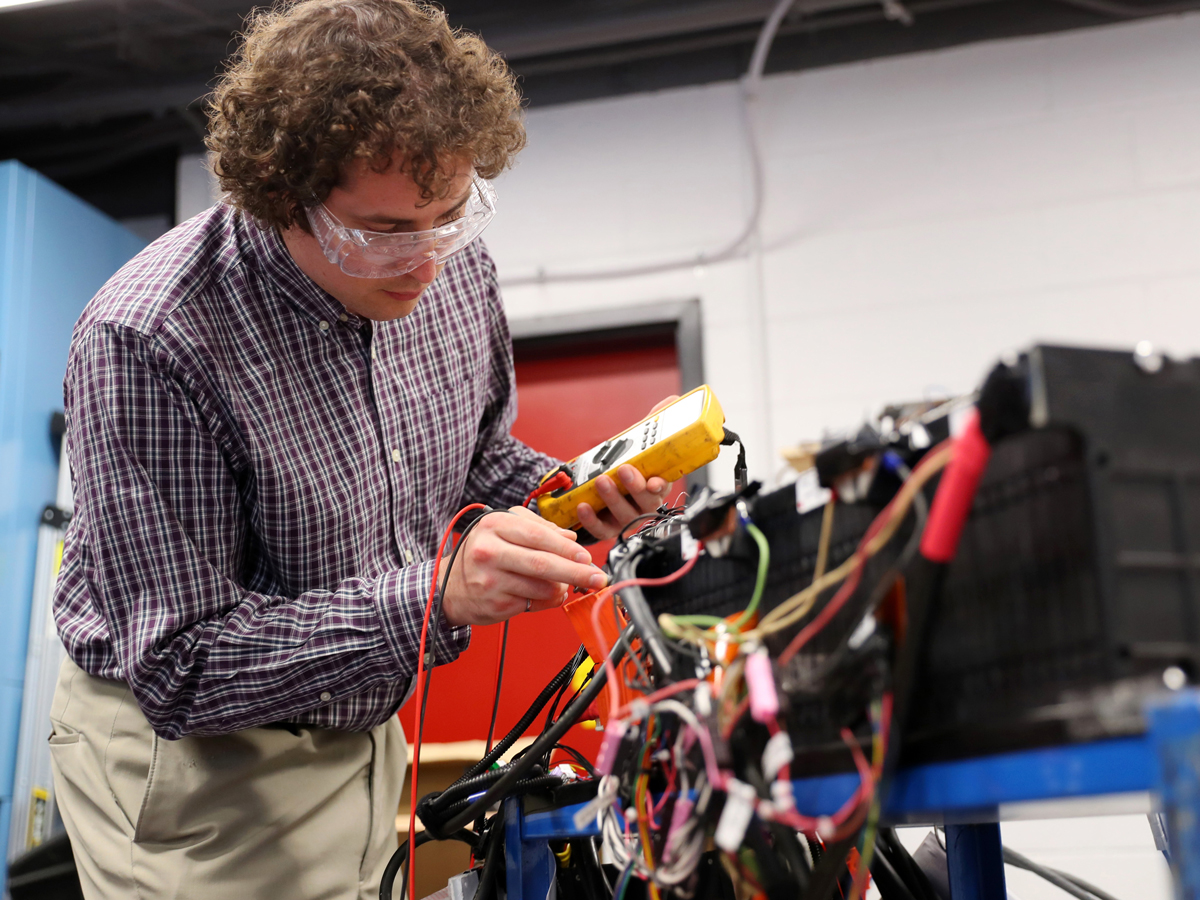 A male researcher with goggles is working on a project with electrical wires.