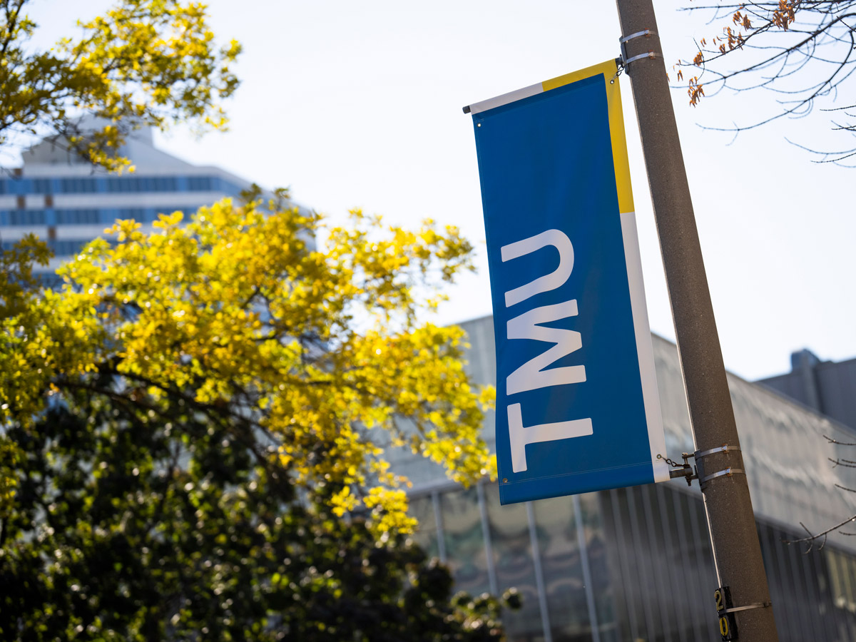 A TMU banner by a tree on campus.