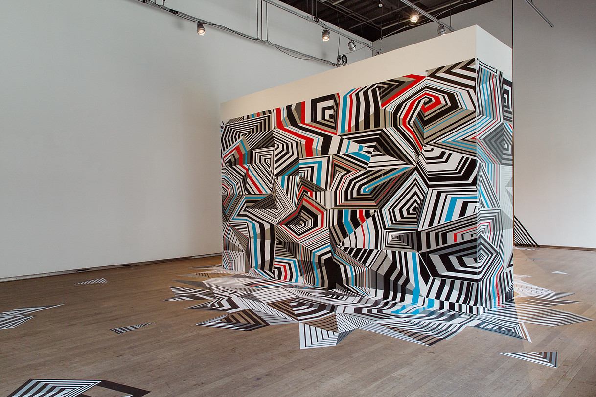 An optical illusion geometric design wrapped around a wall in a gallery space. 