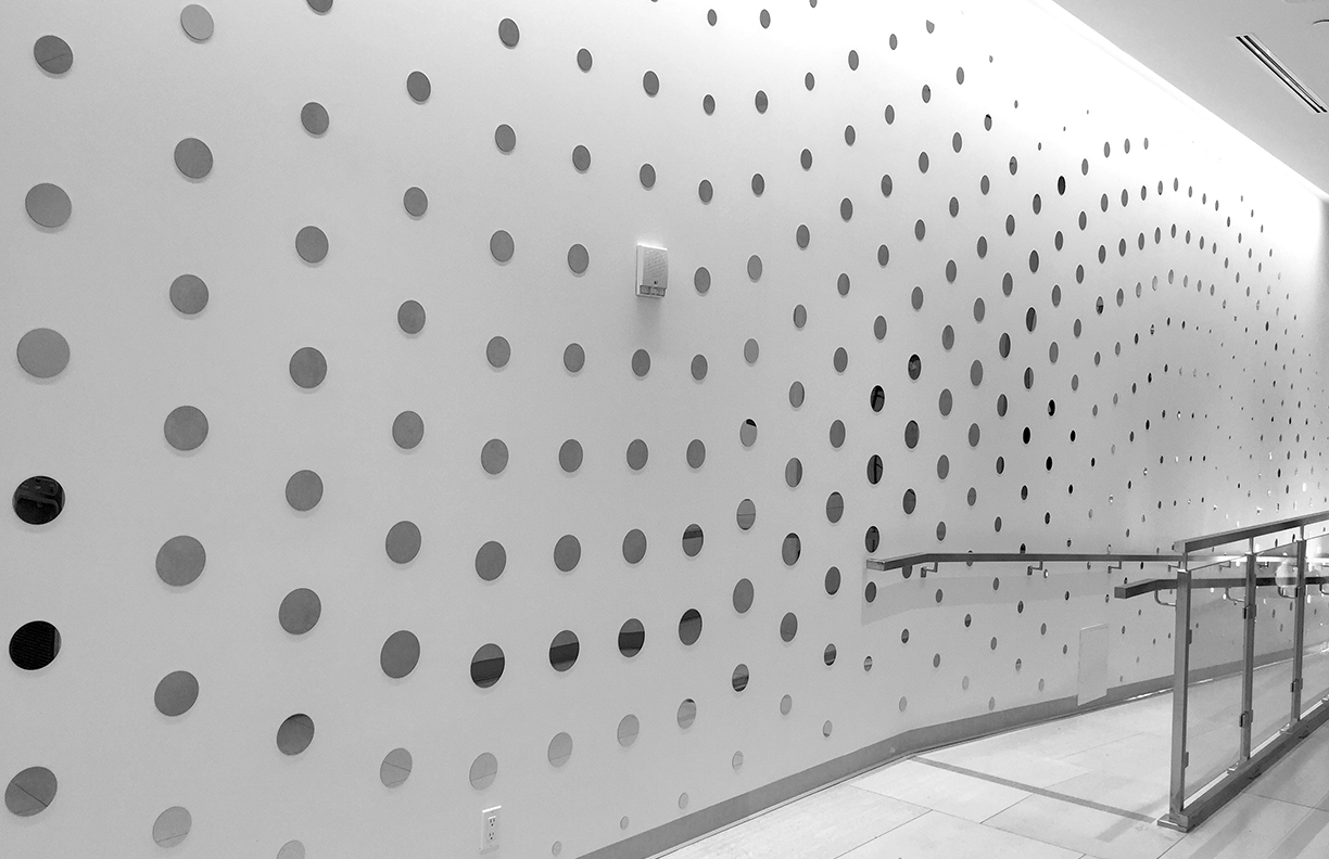 A white corridor. The wall is covered with small circles with imagery printed on them.