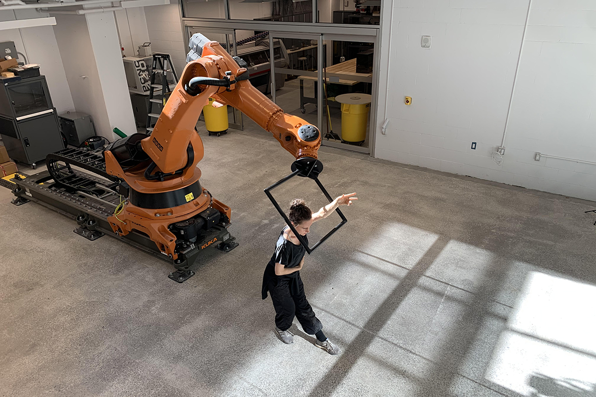 An industrial sized-robotic arm gracefully dances in unison with a female dancer