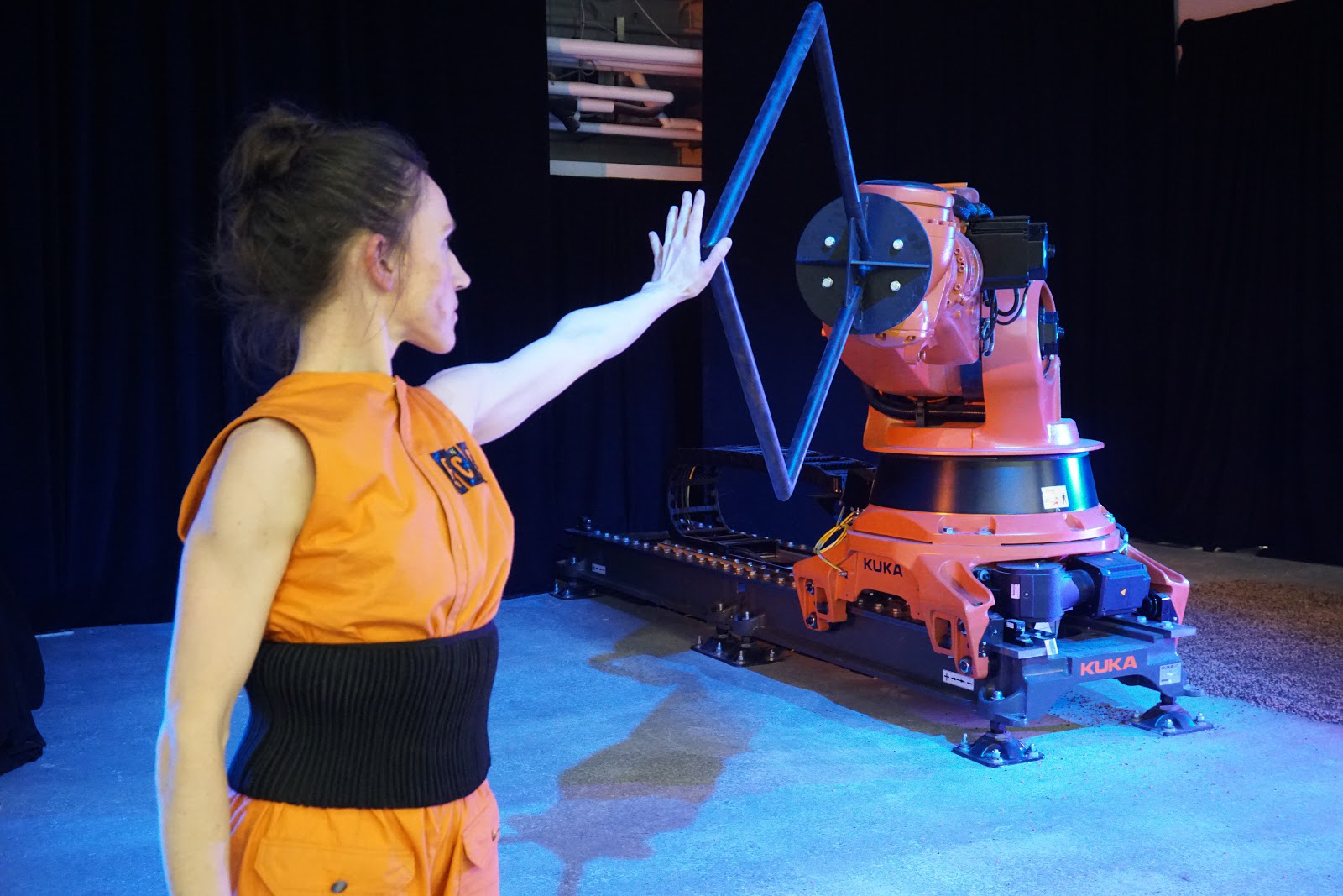 A performer reaches out to an extended robotic arm. 