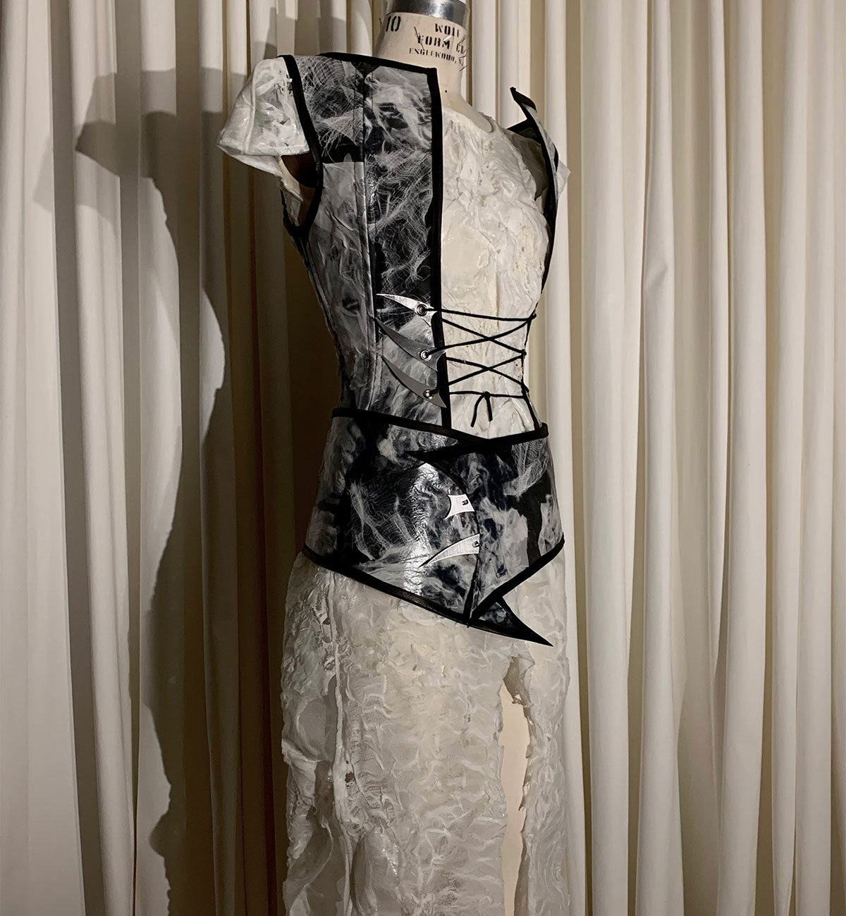 A decorative garment on a mannequin. A marbled-black corset is layerd over a lace white dress.