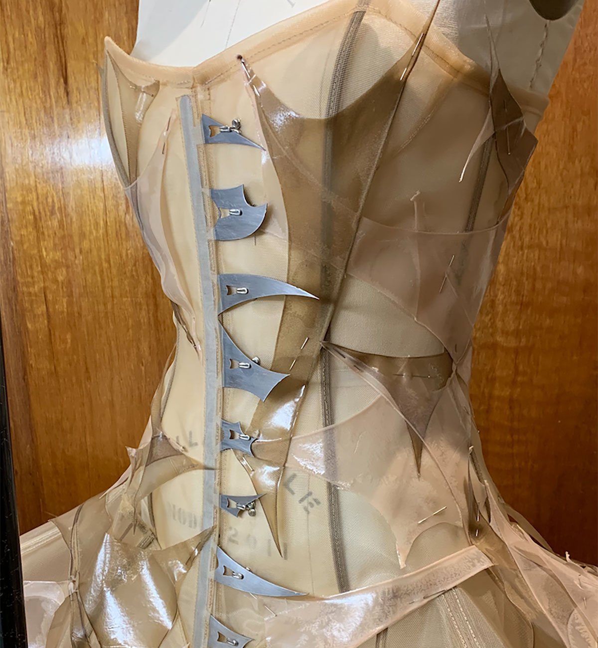 A close-up photo of a corsette on a mannequin. The garment is decorated with sharp-looking, nude-coloured,  abstract shapes.
