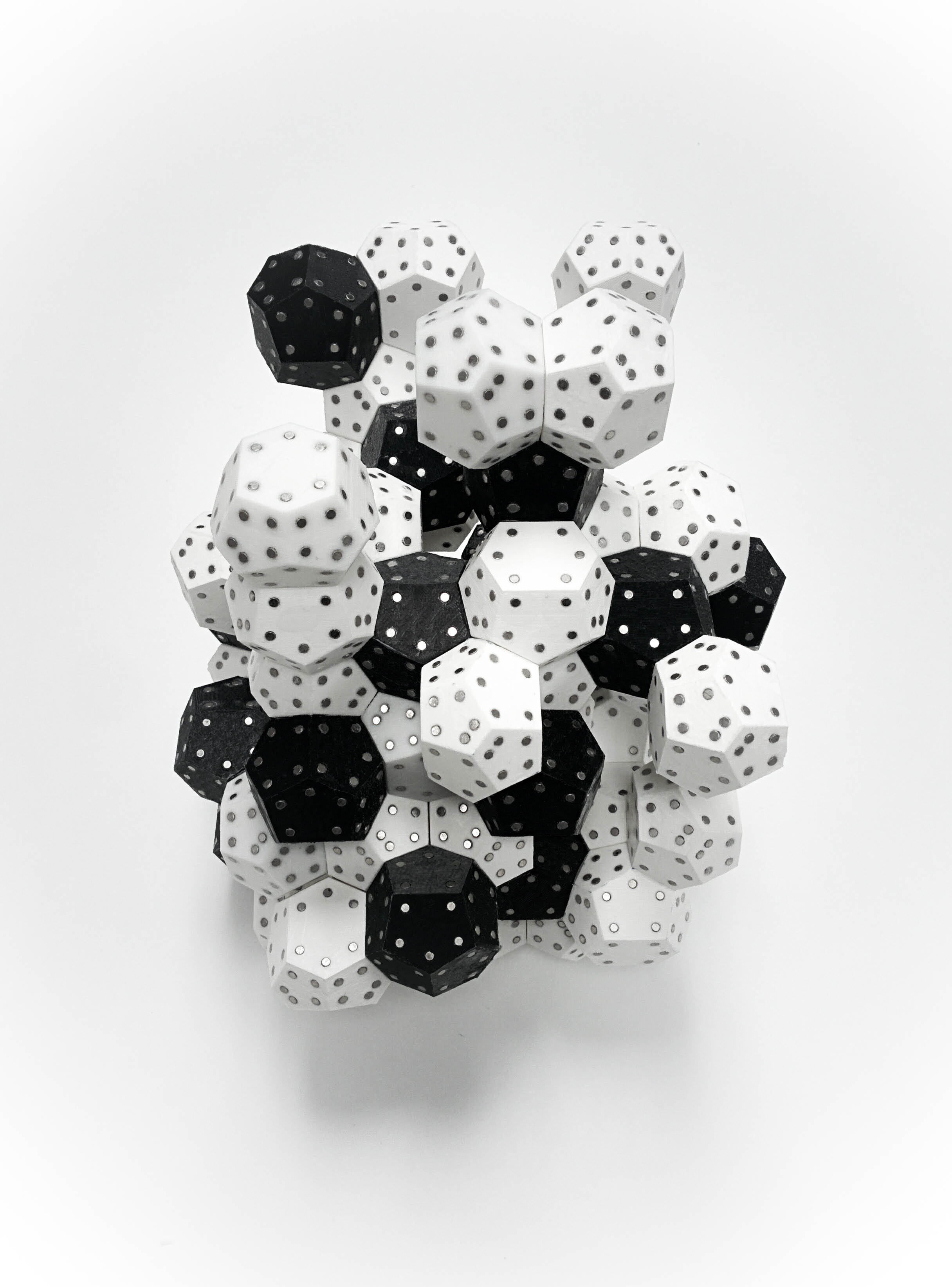 A collection of multi-sided geometric forms. Some black, some white, all with small dots on each face. They are stacked on top of each other to form a clustered structure. 