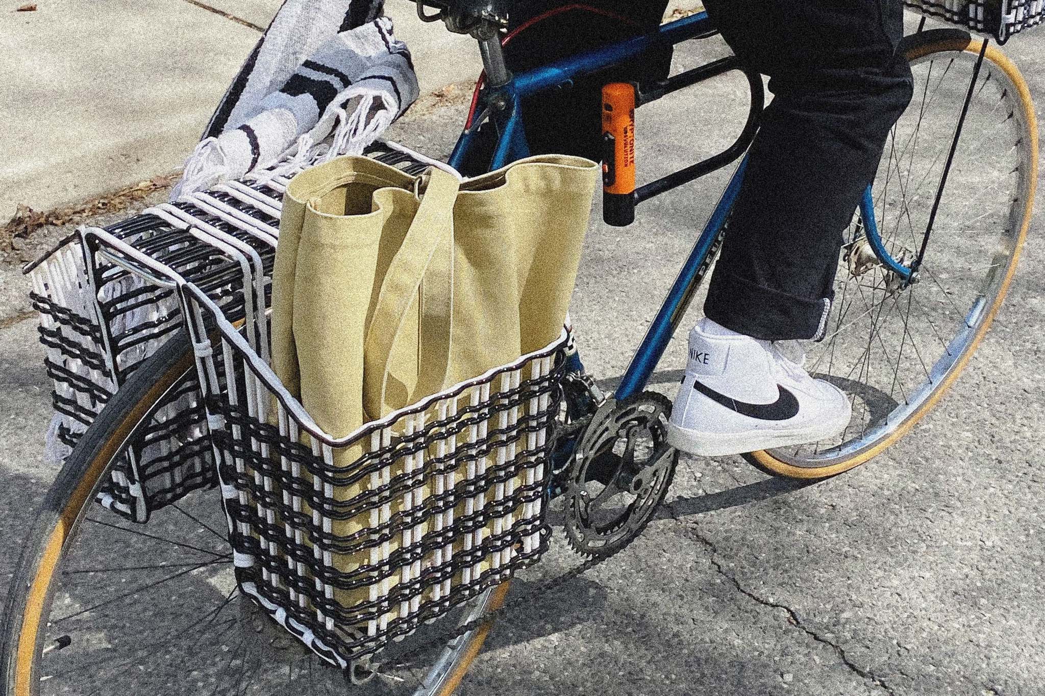 A close-up image of rear bike baskets on a bike. The basket is woven black and white plastic, resembling a textile. One basket is holding a canvas bag.