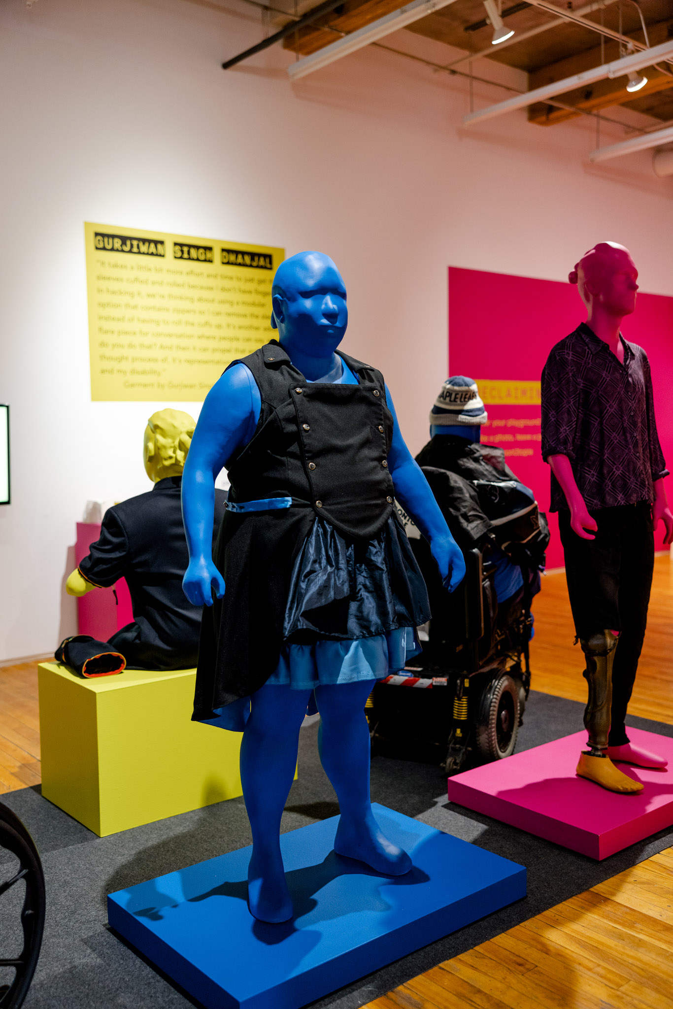 A blue mannequin stands in a gallery setting wearing an A-line, double-breasted black and blue dress. 