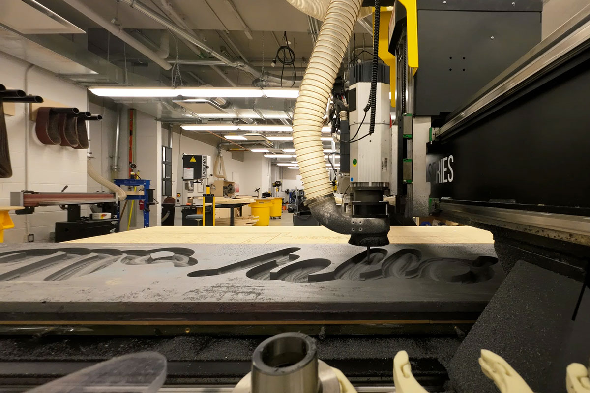 A large-format CNC router carves into grey foam. 