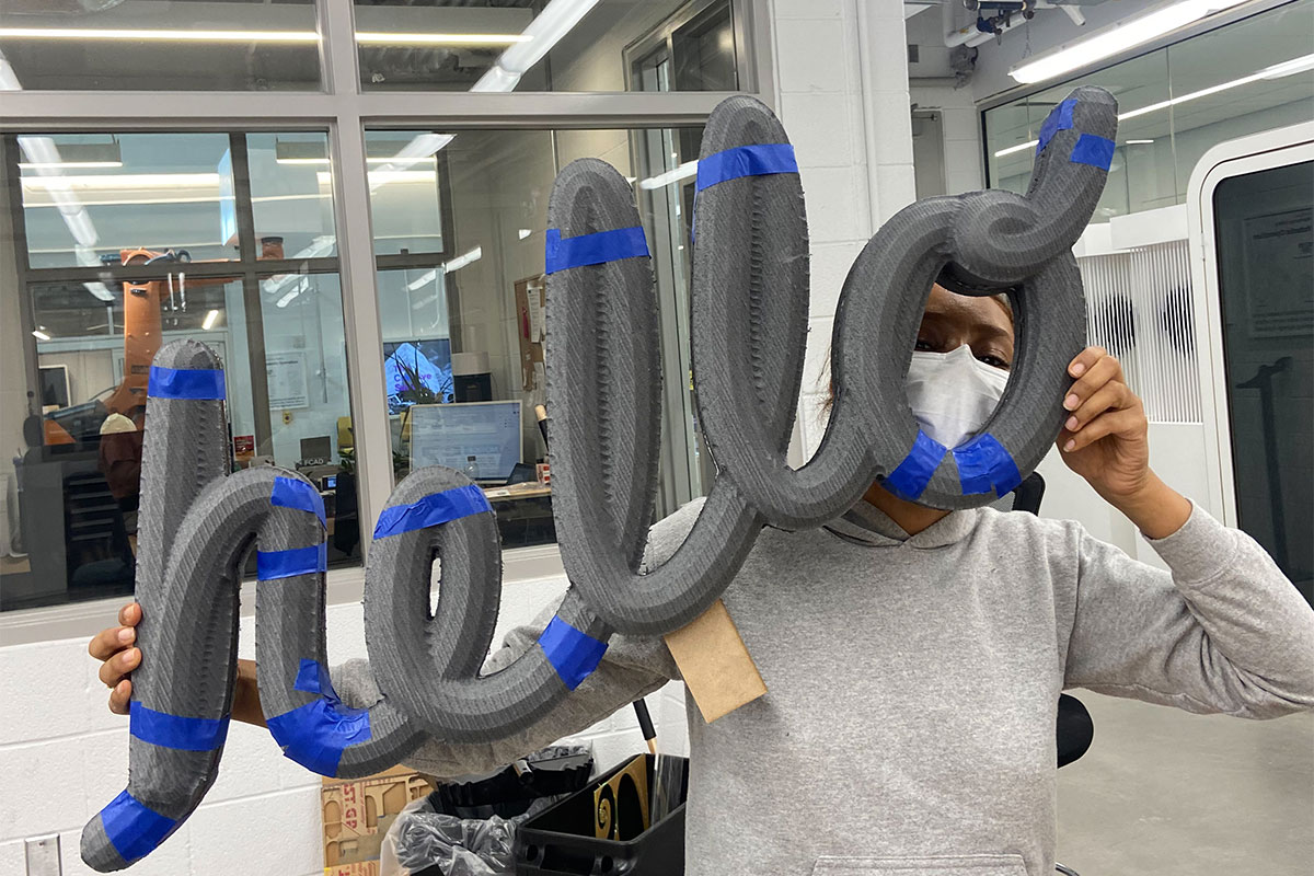 A staff member holds up a sculpture of the word "hello", peeking through the letter "o".