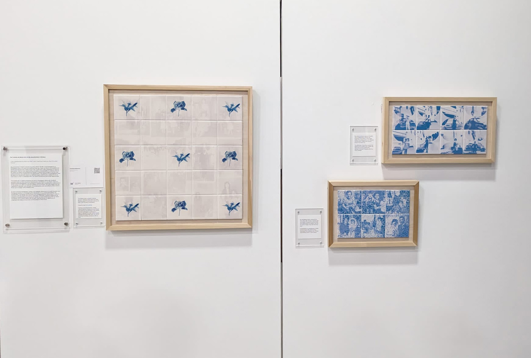 Framed grids of tiles in a gallery setting. Some tile have blue images printed on the surface.. Beside each frame are written descriptions. 