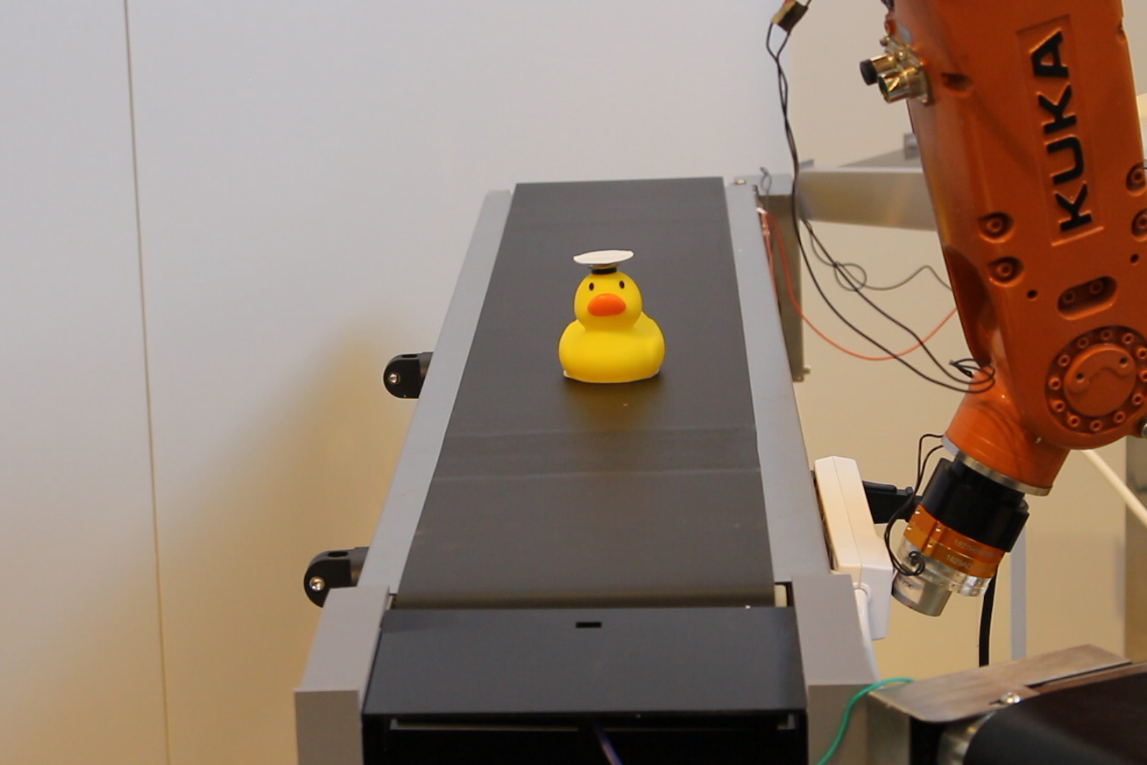 A yellow duck on a conveyor belt. There is a white circular device on top of the duck's head. 