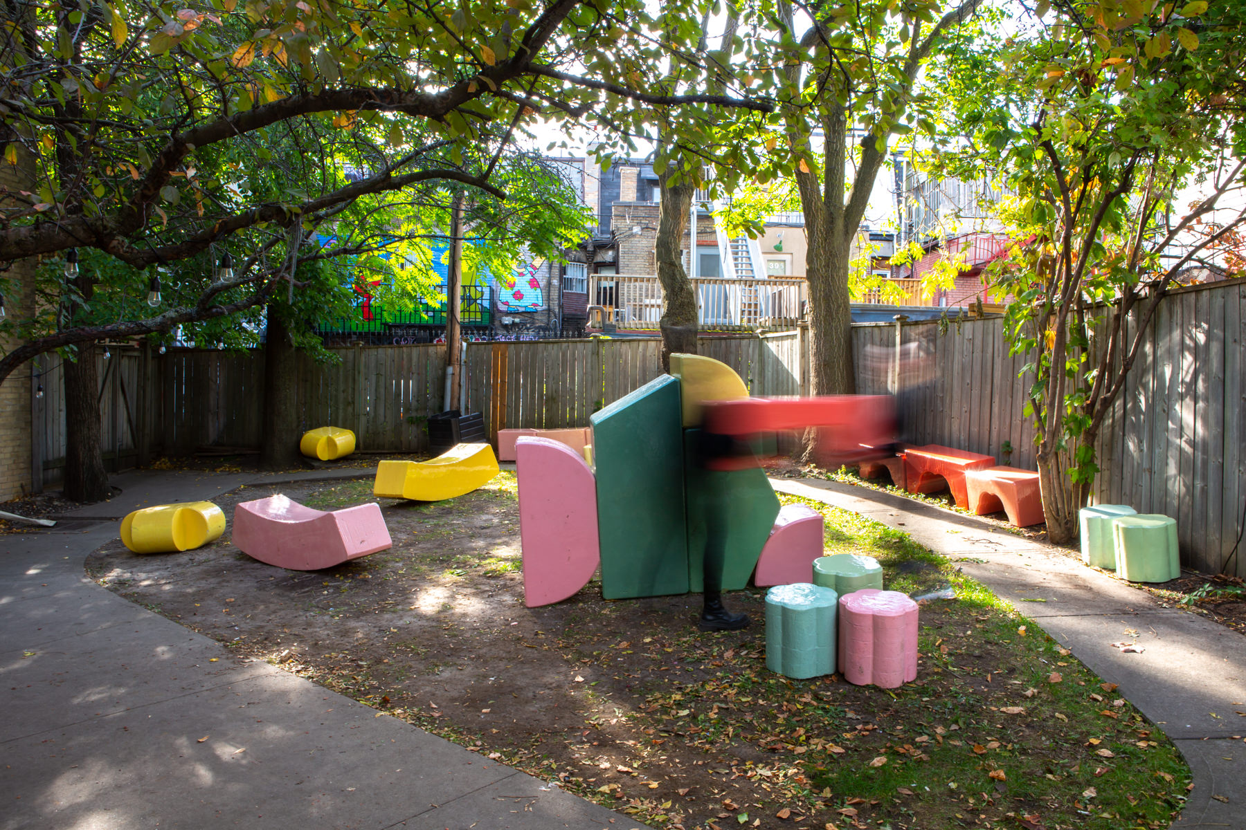 Wide-angle view of about 20 large-scale, colourful blocks from Cecil Community Planting Imagination project. 2 people are photographed moving quickly in front of the blocks.