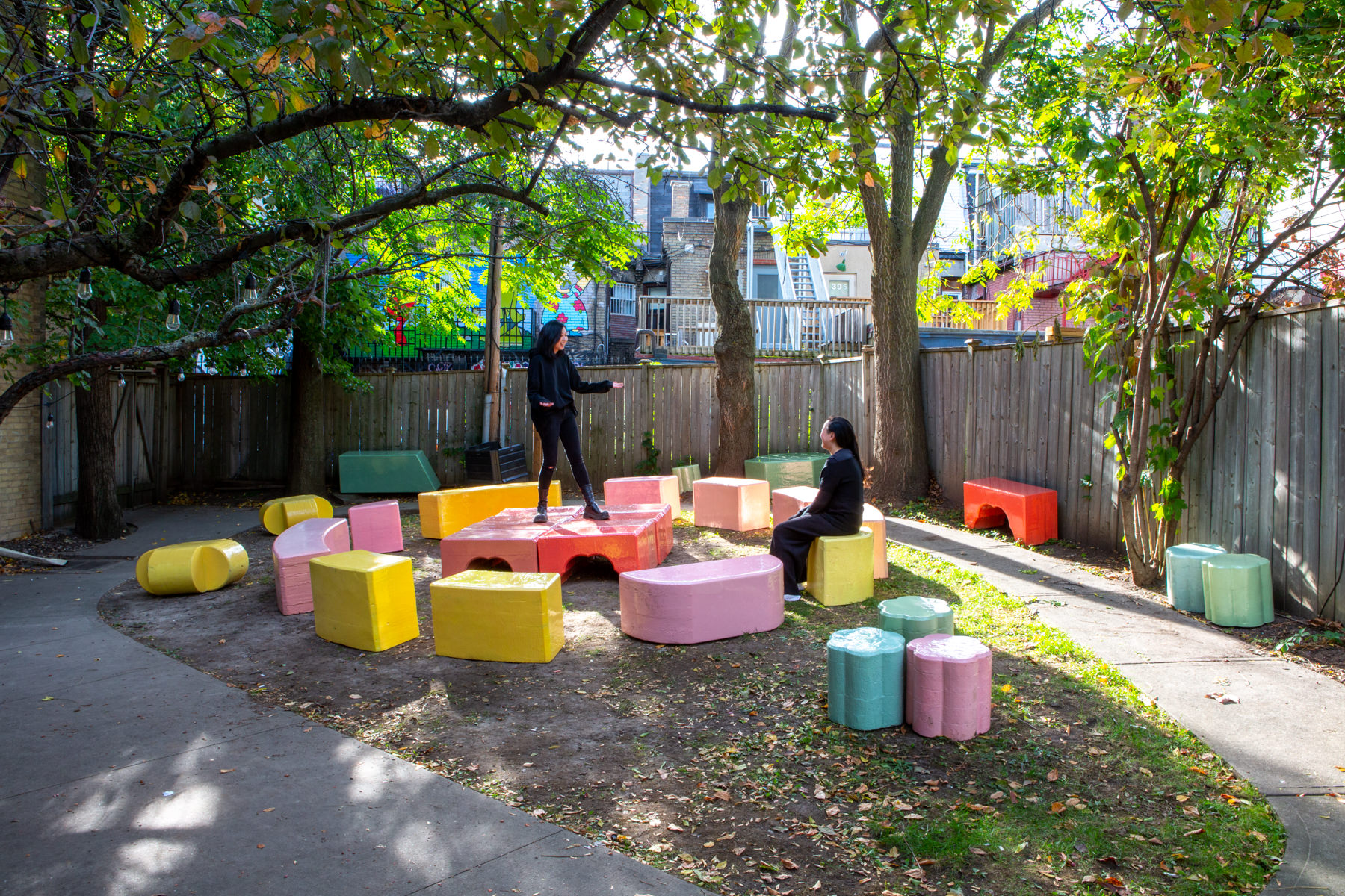 Wide-angle view of about 20 large-scale, colourful blocks from Cecil Community Planting Imagination project. One person sits on blocks looking at someone standing on top of another block.