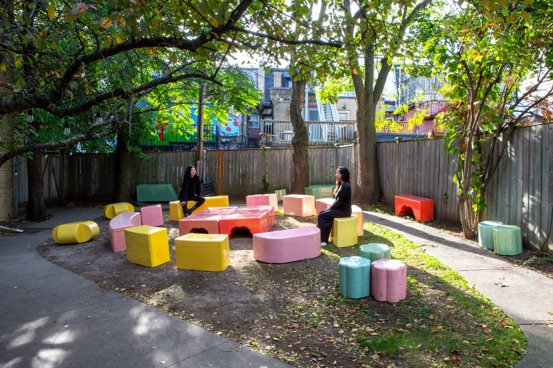 Wide-angle view of about 20 large-scale, colourful blocks from Cecil Community Planting Imagination project. Two people dressed in black sit on 2 different blocks.