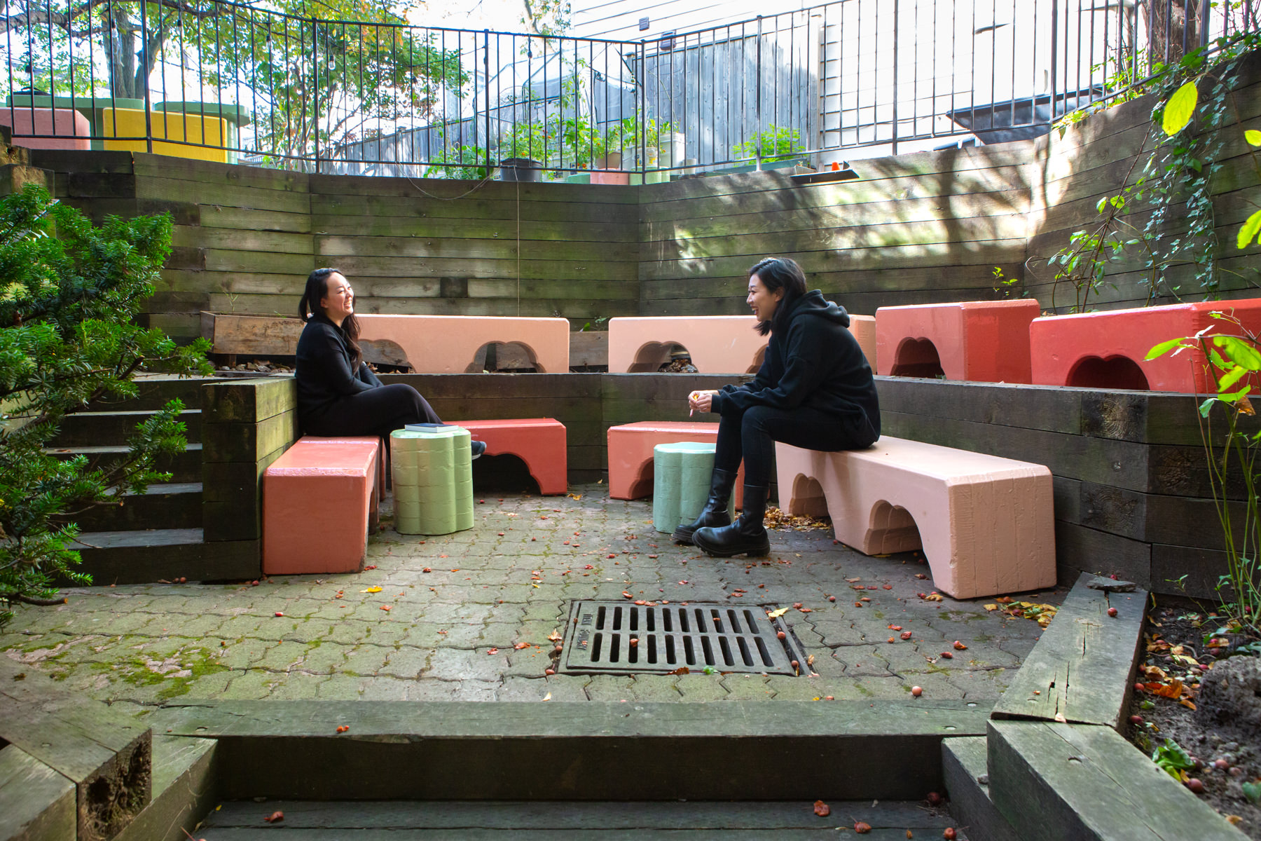 Colourful blacks from Cecil Community Planting Imagination project are neatly arranged in a courtyard. 2 people sit on adjacent blocks in conversation.