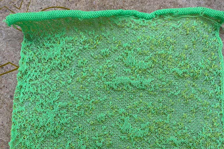 Close-up image of a machine-knit pattern. Bright teal threads are knit together to make a marbled texture.
