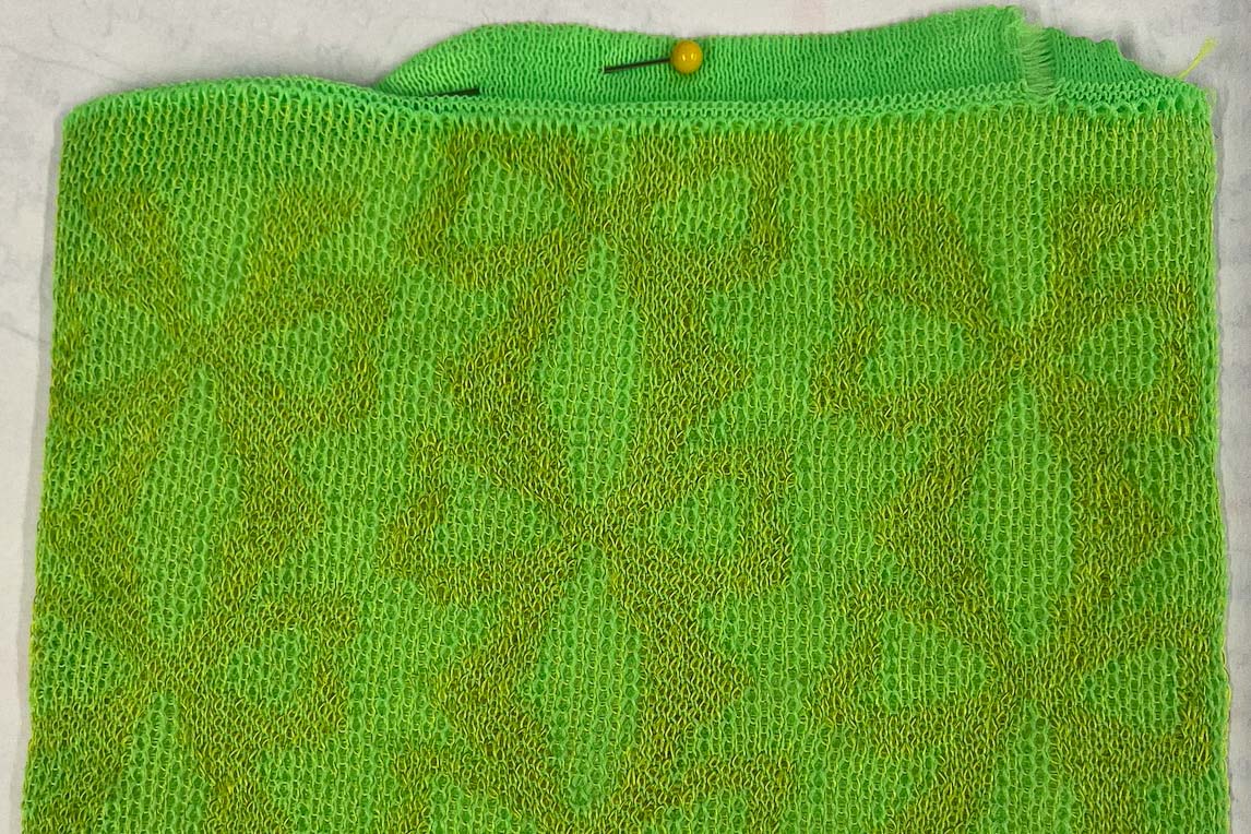 Close-up image of a machine-knit pattern. Neon green and orange threads are knit together into a design of tessellated bows.