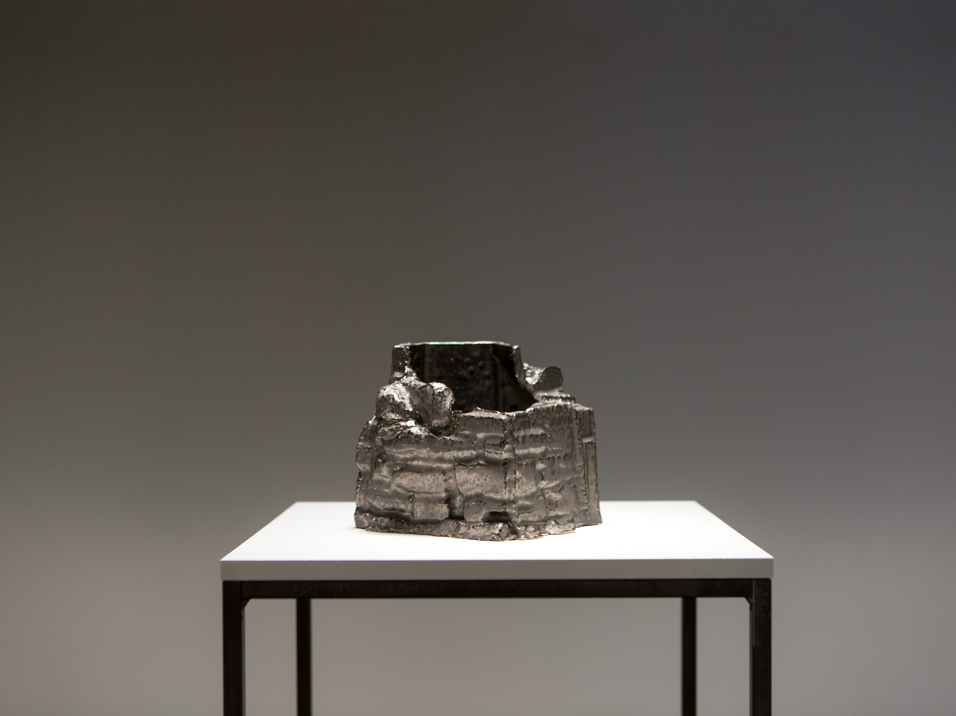 A ceramic form showcase on a plinth. The ceramic is coated with metallic silver glaze.