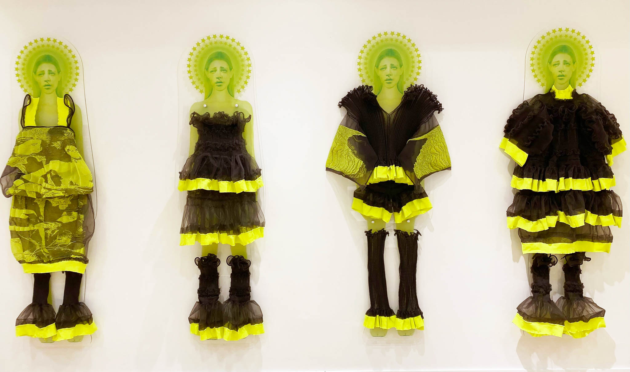 A series of 4 neon green printed women, each wearing different garments from the Veiling Veronicas series. Each neon printed women is mounted to a white wall as if they're floating.