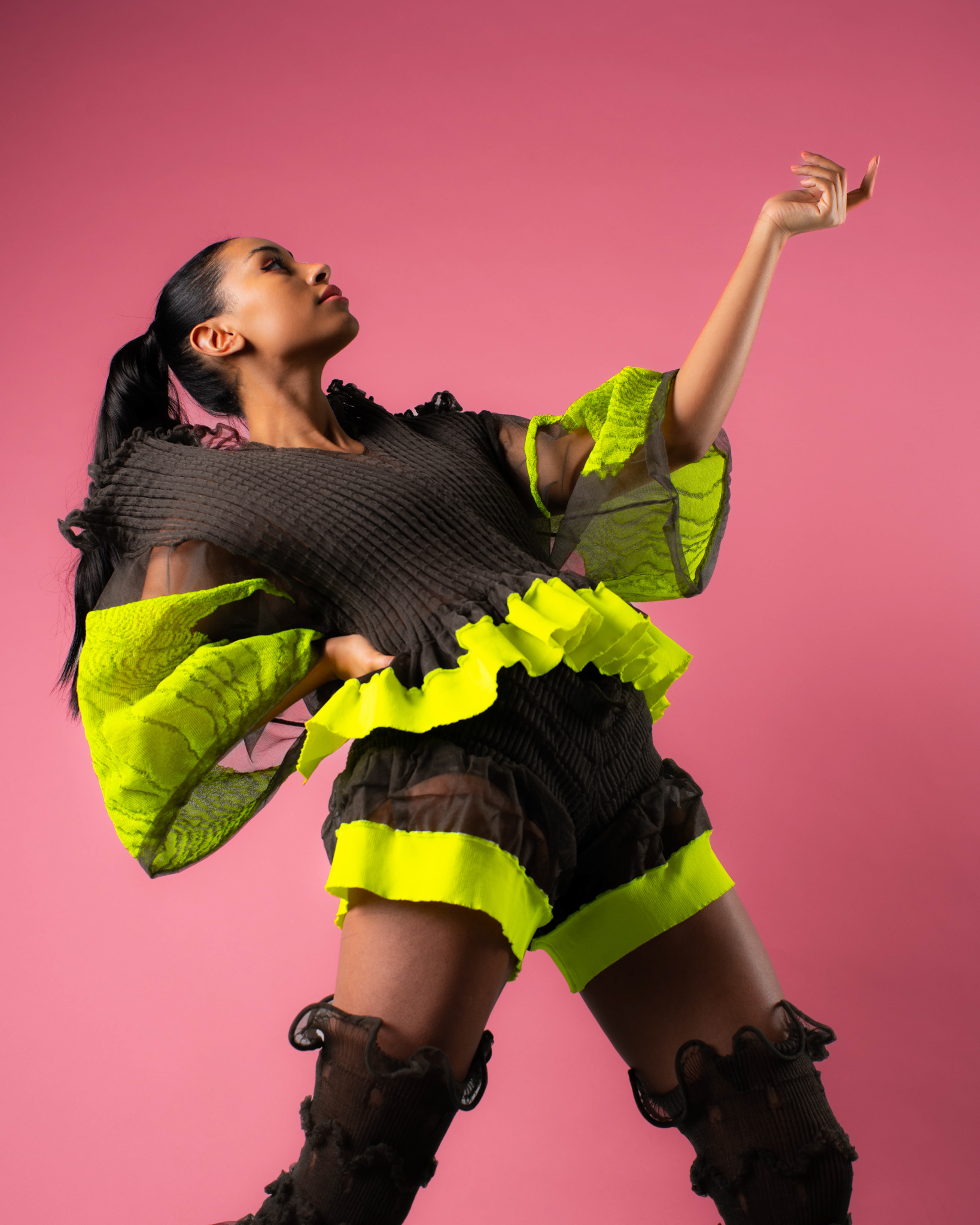 Fashion model posing leaning backwards and pointing her arm upwards. Pink backdrop. Showcasing one of the garments from Veiling Veronicas series.