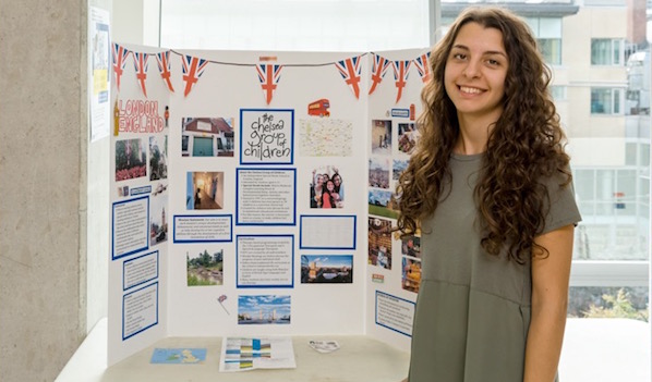 Vasiliki Victoria Rombos is standing near the banner of the Chelsea Group of Children, England