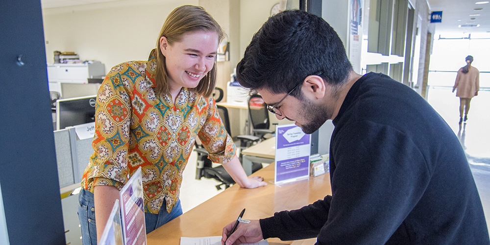 Student filling out a form at the first-year engineering office with a smiling staff member behind the counter