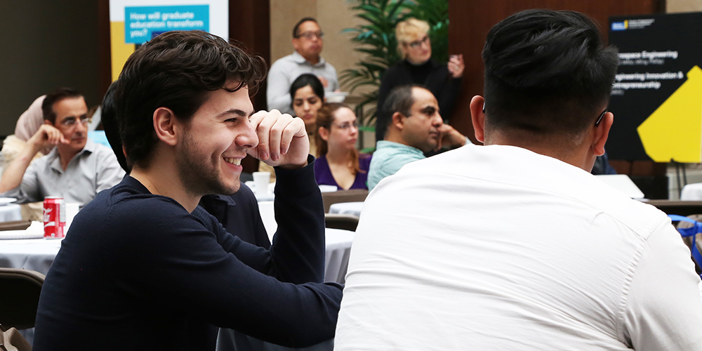 A graduate student smiling at a table during a conference