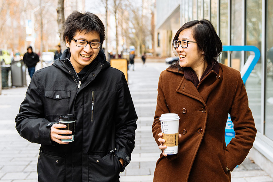 Two students walking and drinking coffee.