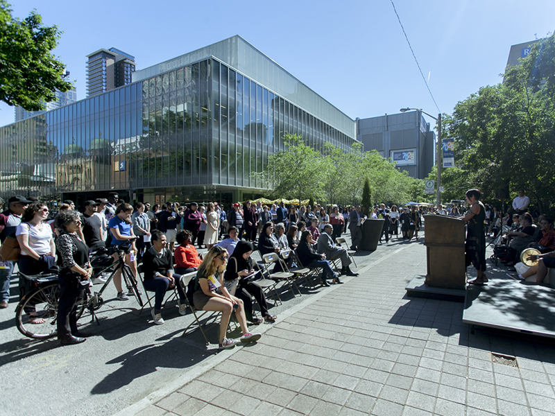 Ryerson community members gather on Gould Street, listening to a person at a podium at the plaque unveiling for next to the Egerton Ryerson statue on Gould Street 