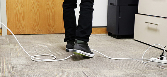 A person's foot close to getting caught on a wire stretched across the floor. 
