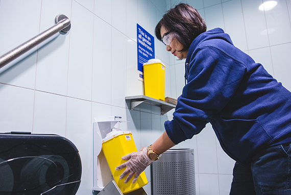 A member of the Facilities Management and Development team safely chaining the sharps disposal container in a washroom. 
