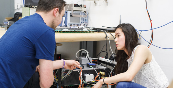 Two students looking at wires on a piece of electrical equipment.