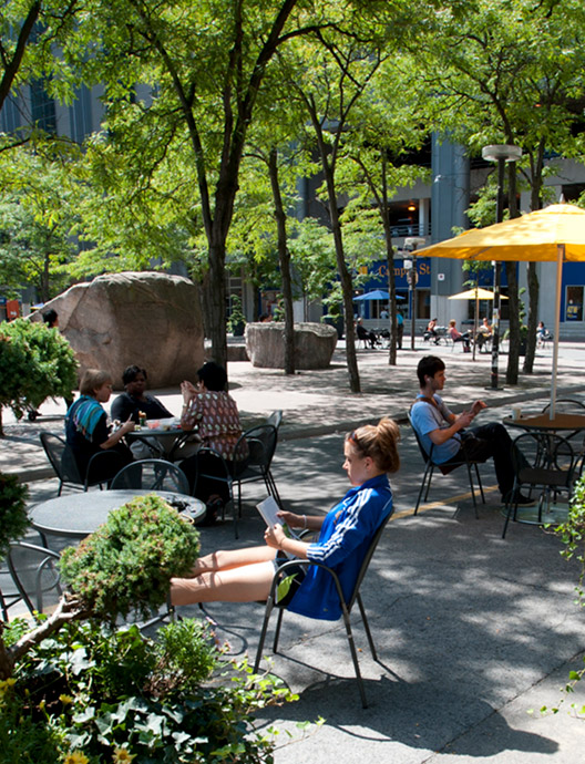 Students sitting at tables along Gould Street with green planters and trees around them.