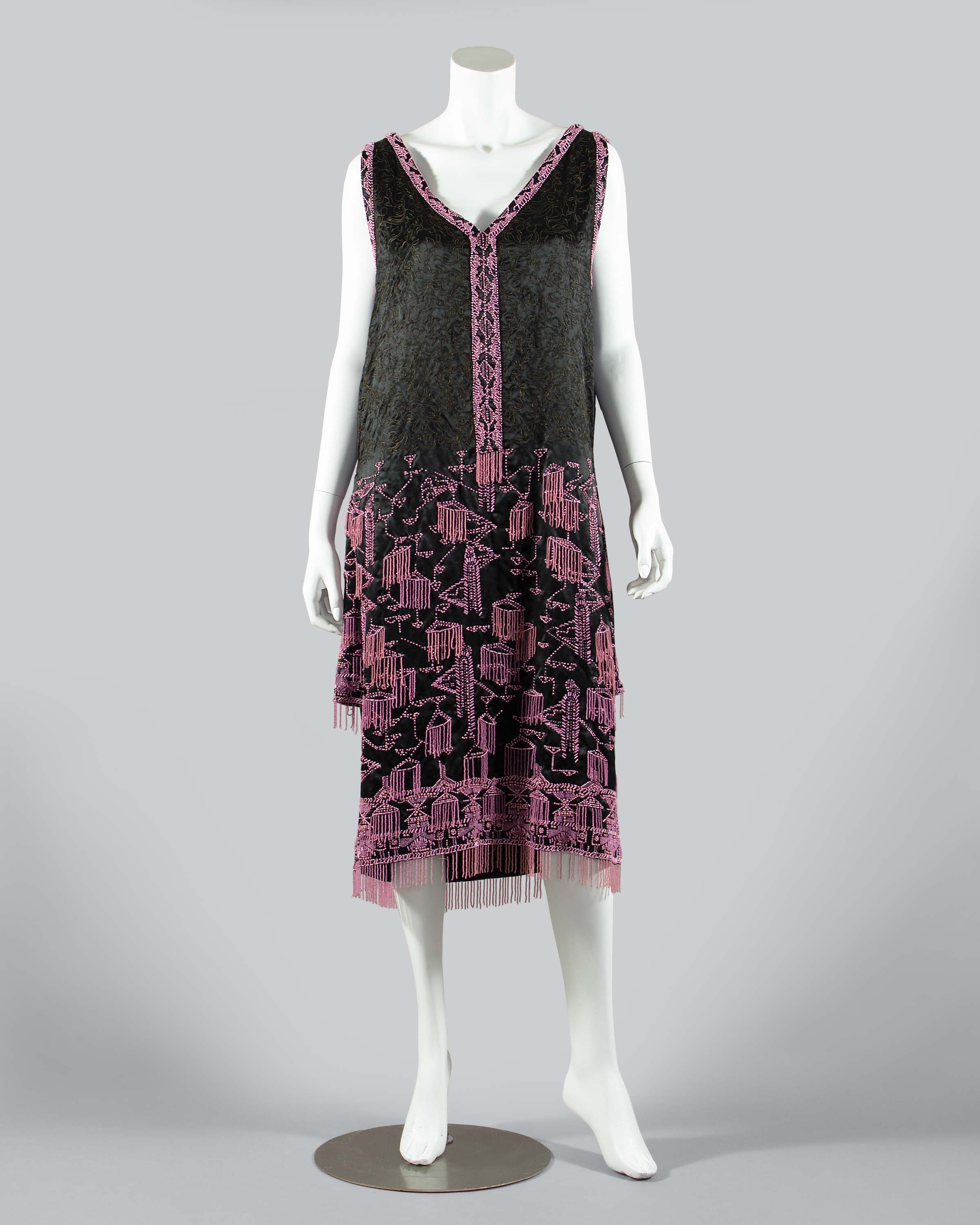 Mannequin wearing a black satin sleeveless dress embroidered with narrow gold cord and pink beads