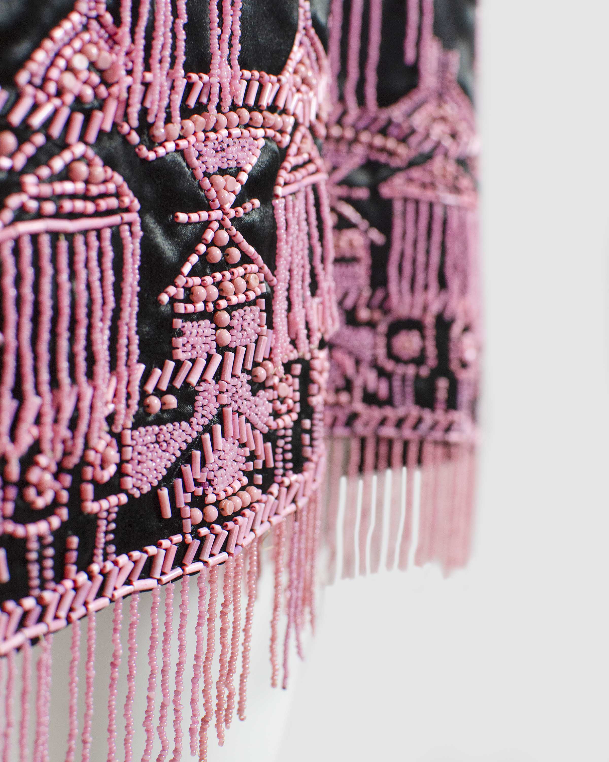 Detail photograph of the beading on the trim of a black satin sleeveless dress embroidered with narrow gold cord and pink beads